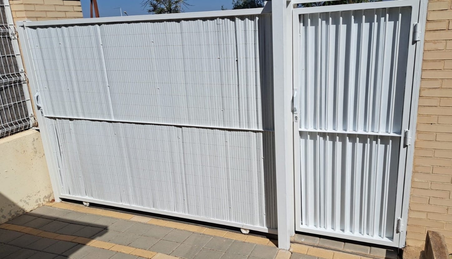 Puerta metálica corredera blanca con acceso peatonal integrado